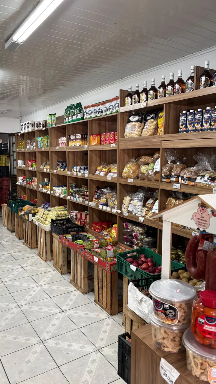 Prateleiras de madeira com pães, conservas e mercearia, e caixotes de madeira com frutas no chão